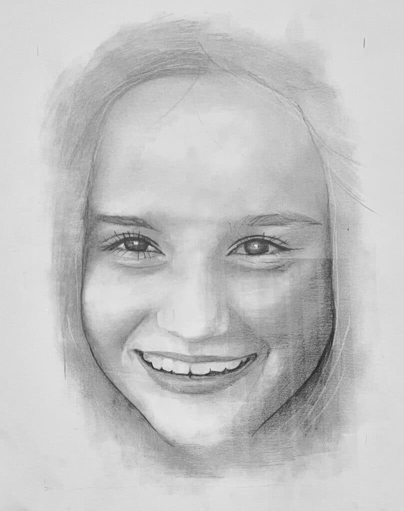 A pencil sketch of a smiling young persons face, showing expressive eyes, detailed teeth, and subtle shading for depth and texture on the hair and skin. The portrait has a soft, unfinished border blending into the background.